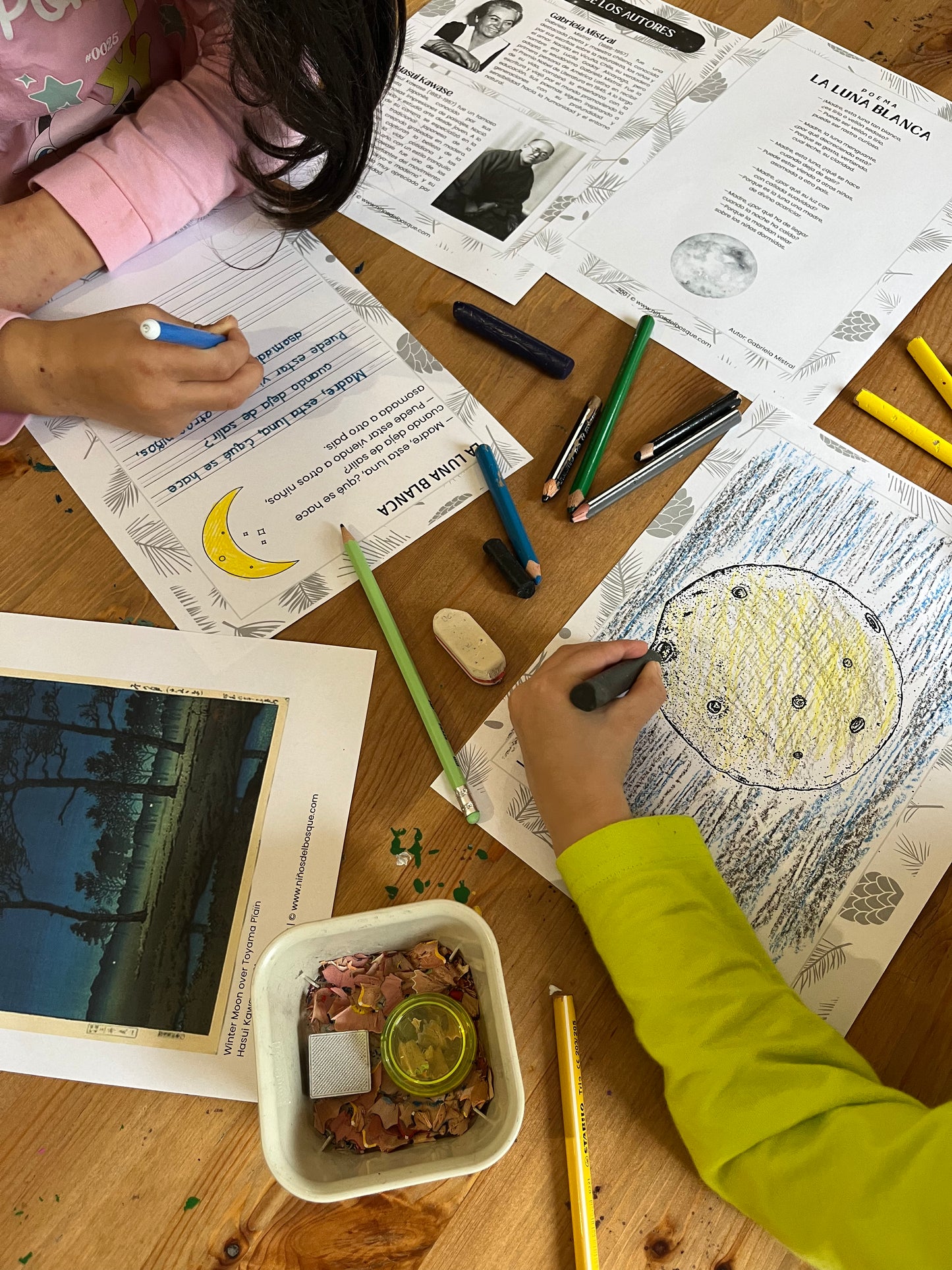 Niños realizando una actividad educativa sobre las fases de la luna, coloreando fichas de naturaleza con lápices y materiales sobre una mesa de madera.